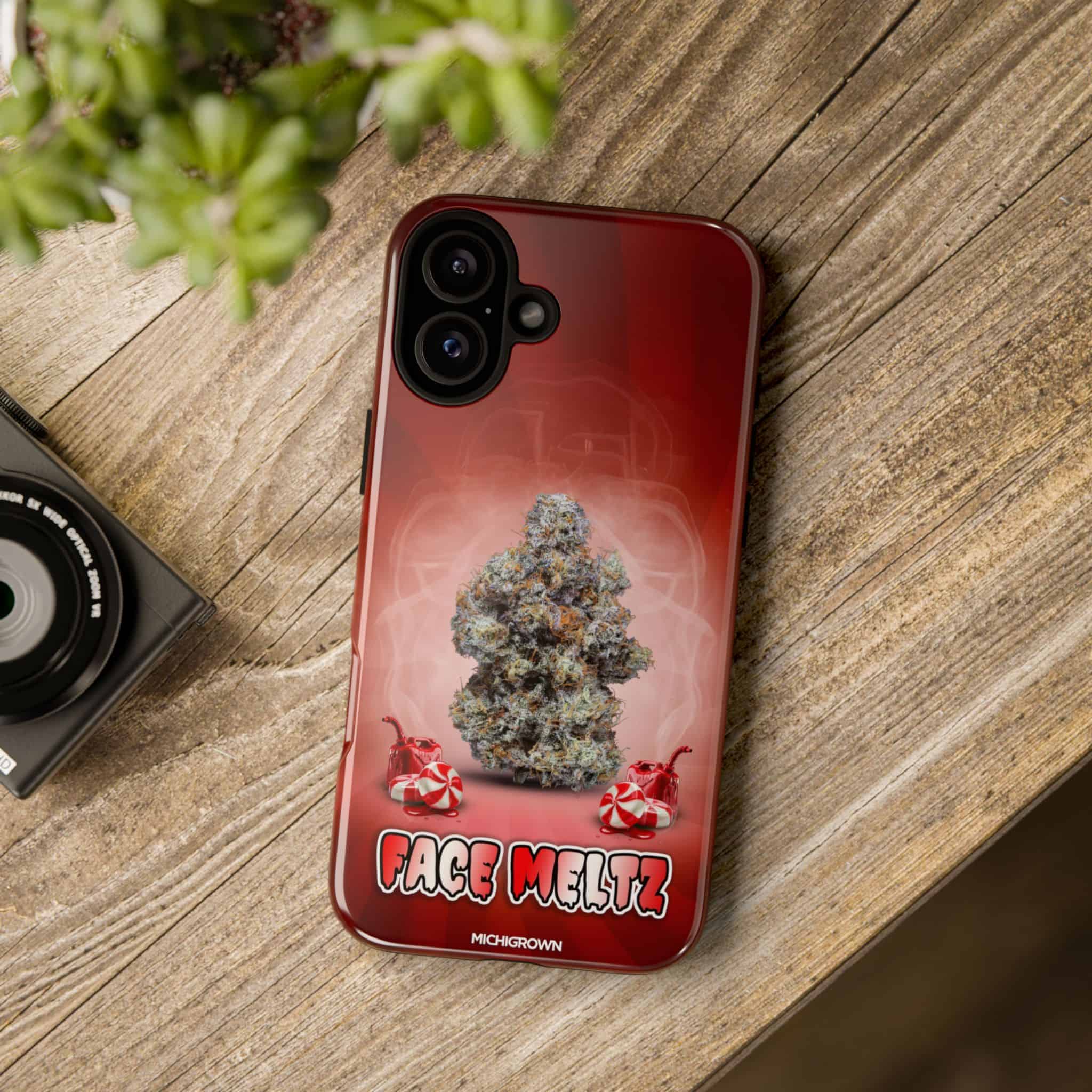 Red phone case with cannabis bud and Face Meltz logo on wooden surface.
