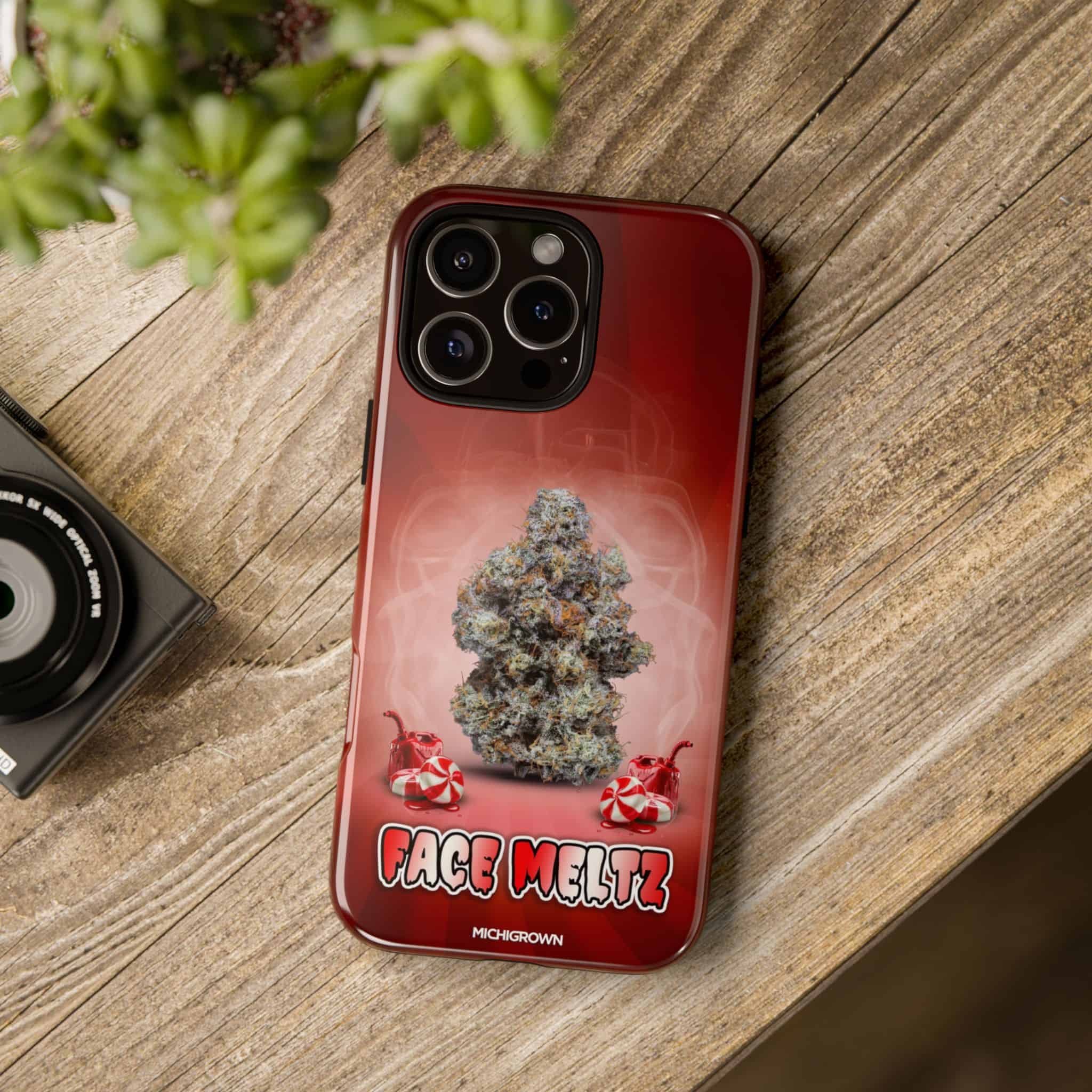 Red phone case with Face Meltz cannabis strain graphic on wooden surface.