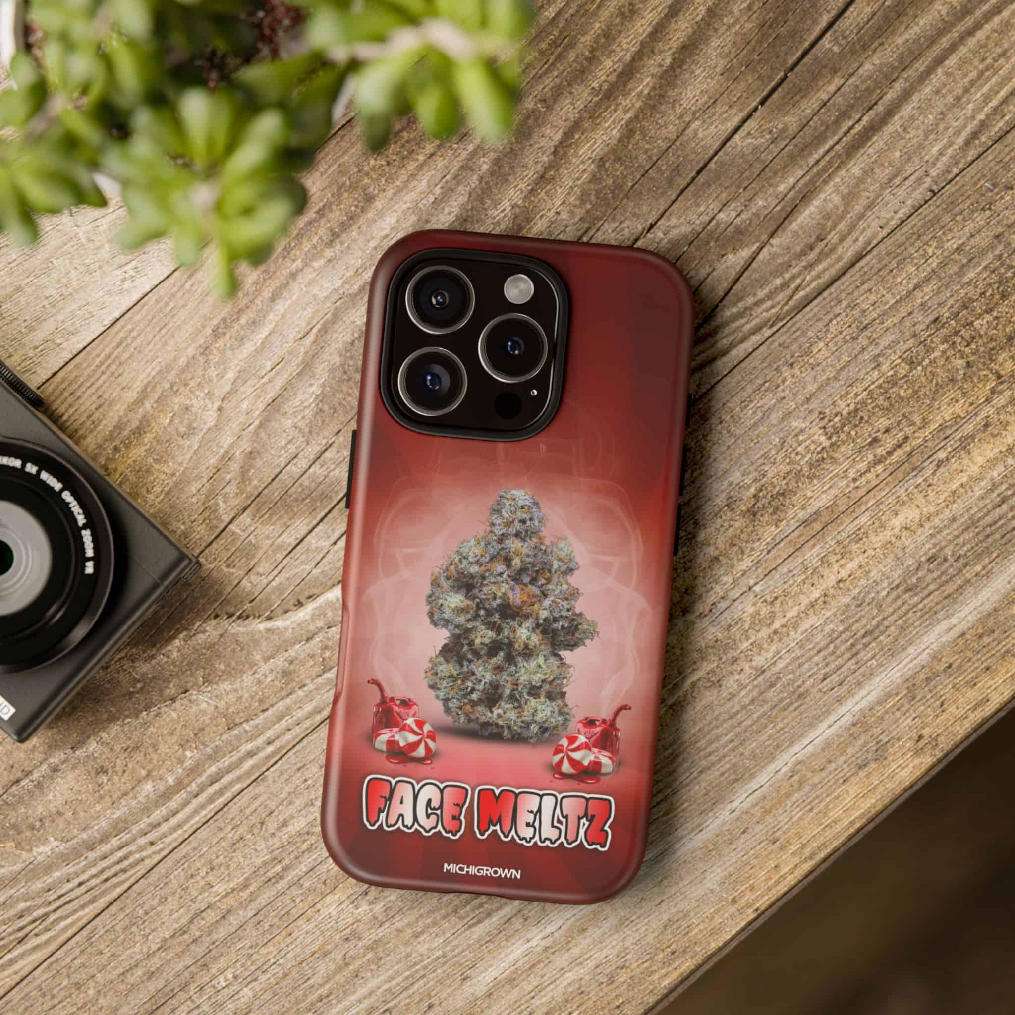 Phone case with cannabis bud design and FACE MELTZ logo on wooden surface.
