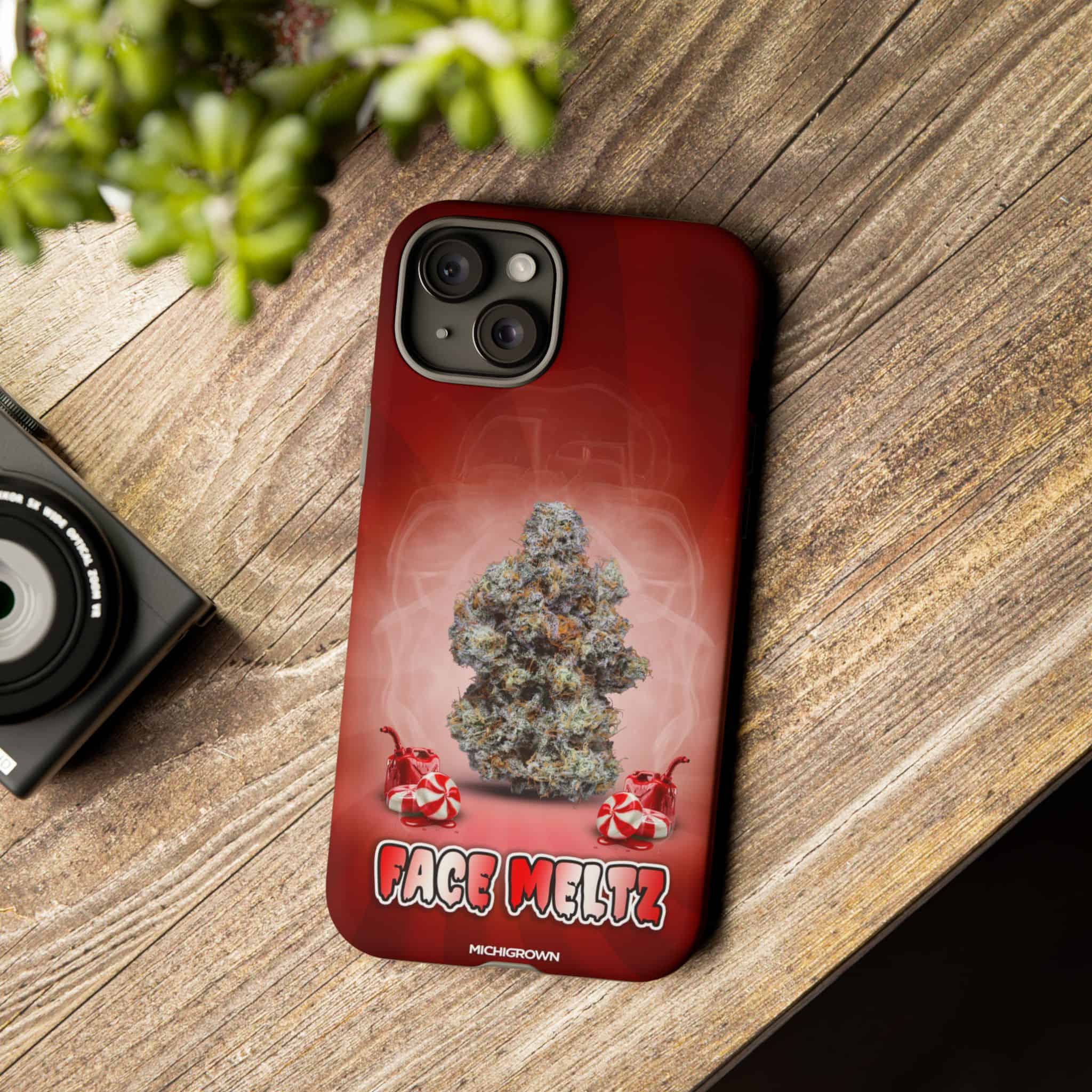 Red phone case with cannabis bud and Face Meltz logo on wooden surface.