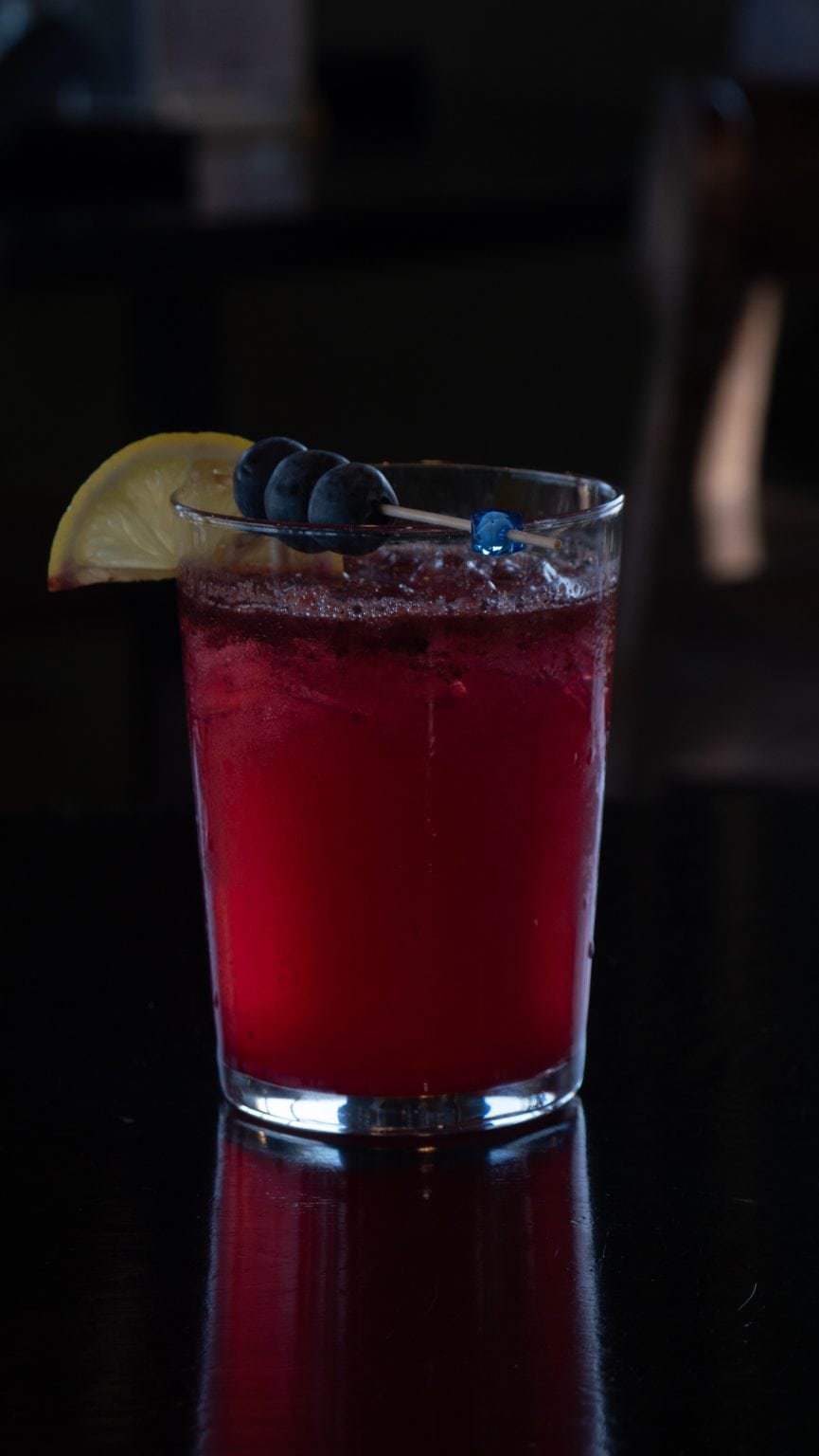Refreshing berry cocktail with lemon wedge, blueberries, and ice in a glass.