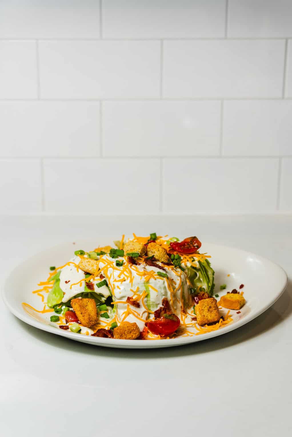Wedge salad with iceberg lettuce, bacon, tomatoes, cheddar, scallions, croutons, and ranch dressing.