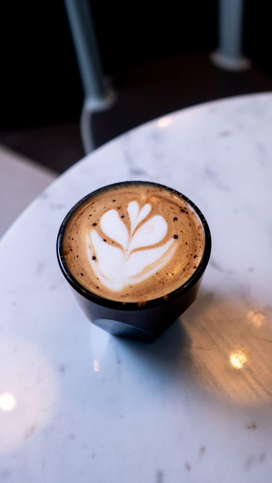 Latte with intricate heart-shaped foam art on a marble table at Mudpenny.