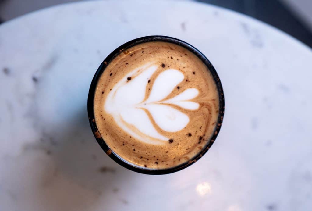 Latte art coffee in a black cup on white marble surface.