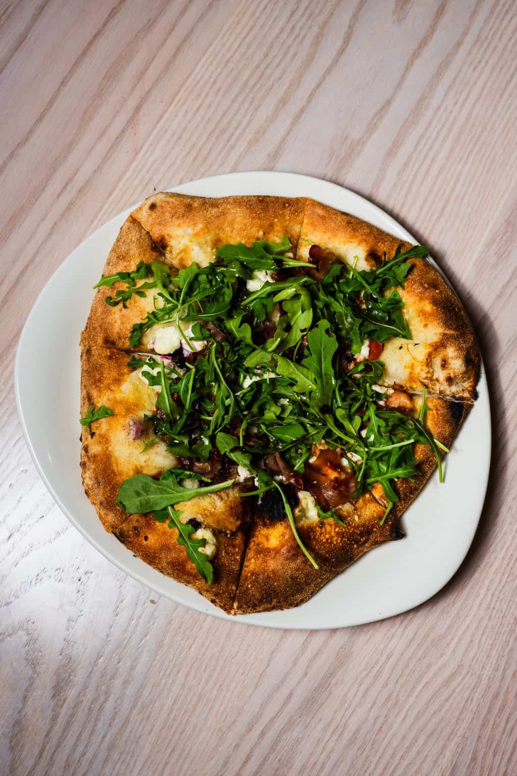 Delicious mushroom pizza topped with fresh greens on a white plate.