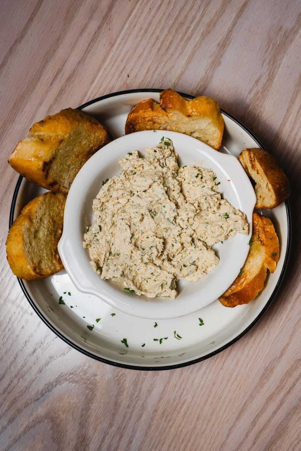 Creamy whitefish dip served with toasted baguette slices on a white plate.