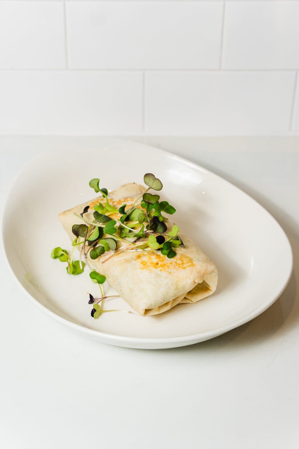 Fresh spring roll garnished with microgreens on white plate.