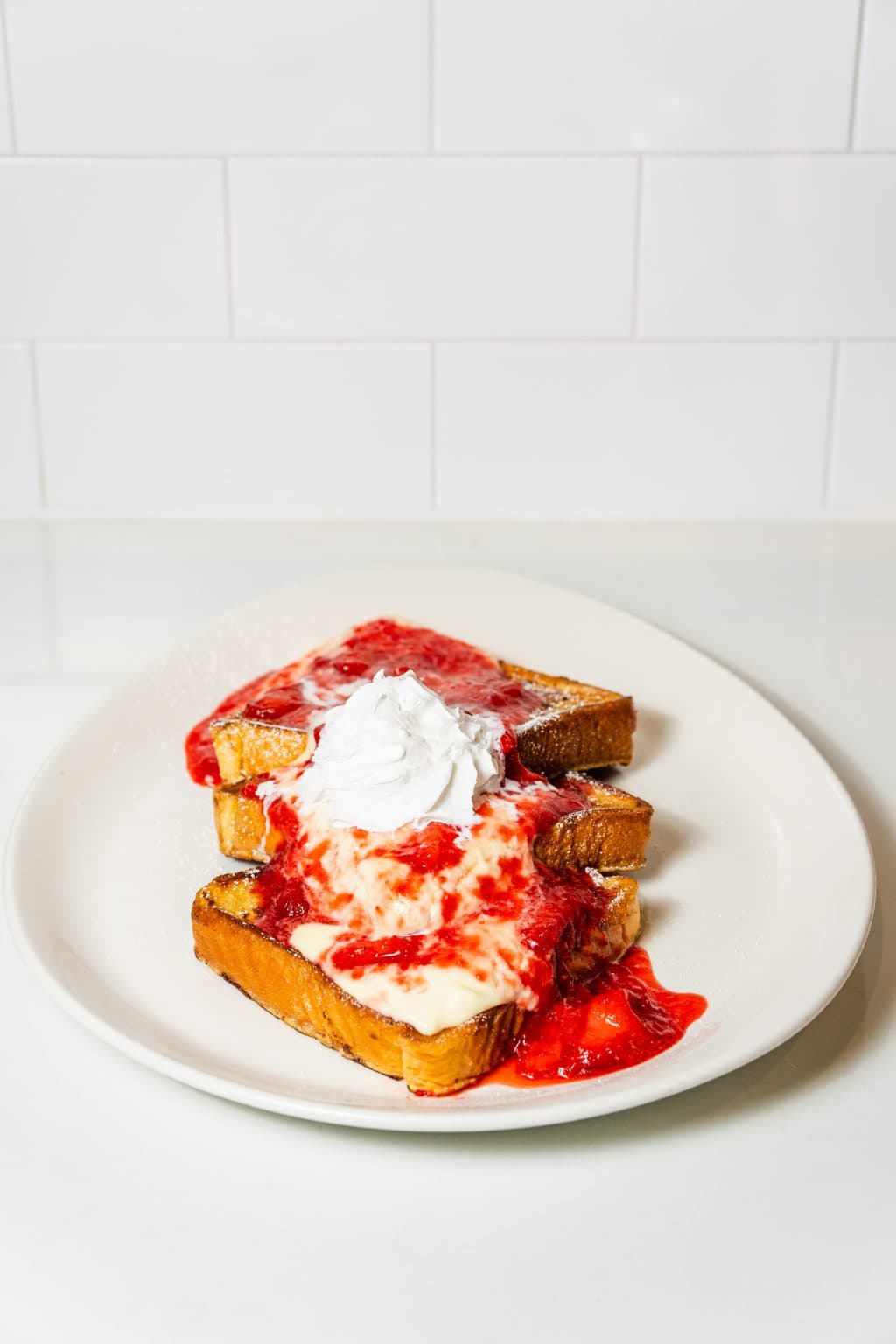 Delicious strawberry cheesecake French toast with whipped cream on white plate.