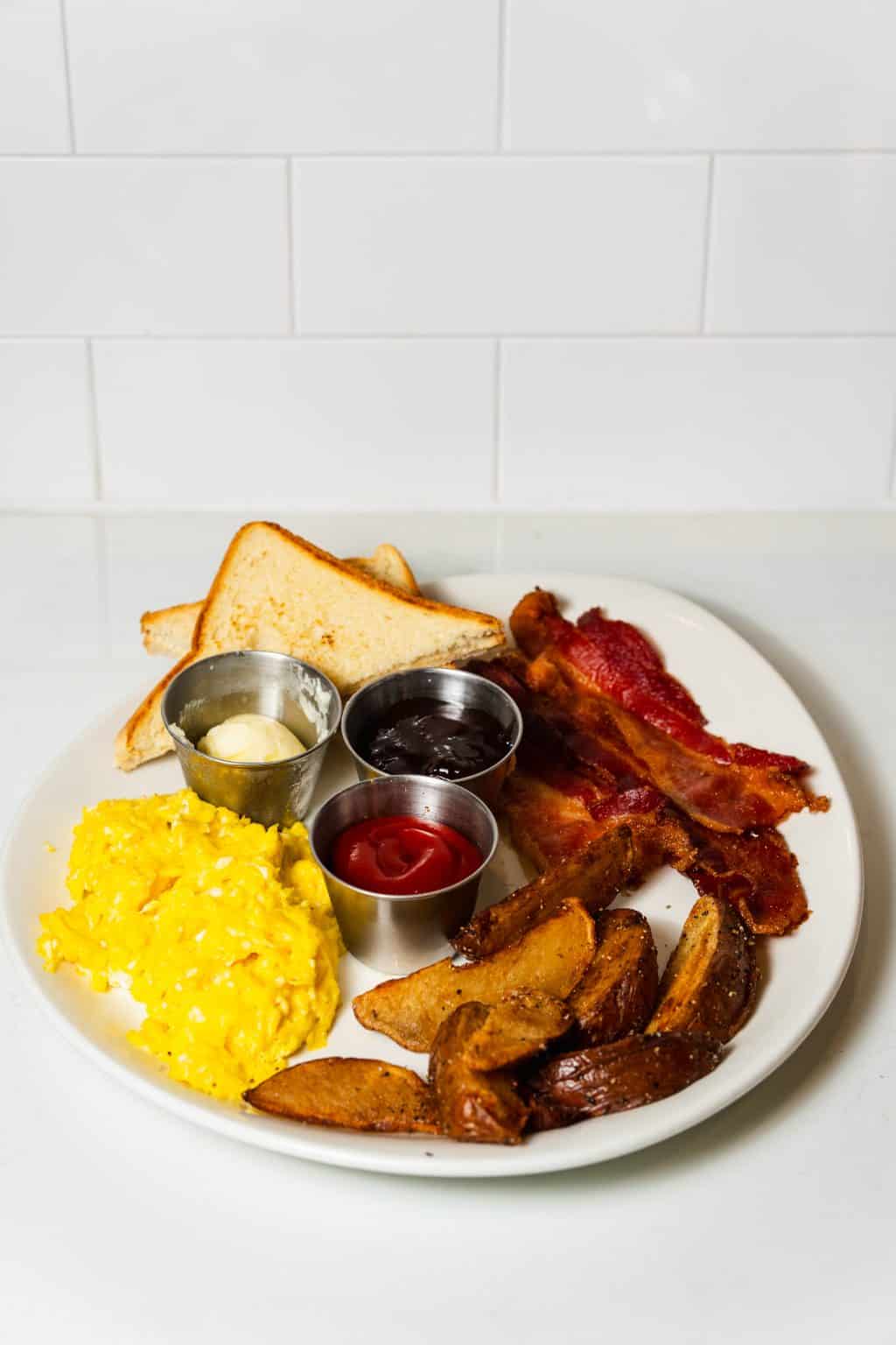 Traditional breakfast with bacon, scrambled eggs, toast, and potato wedges.