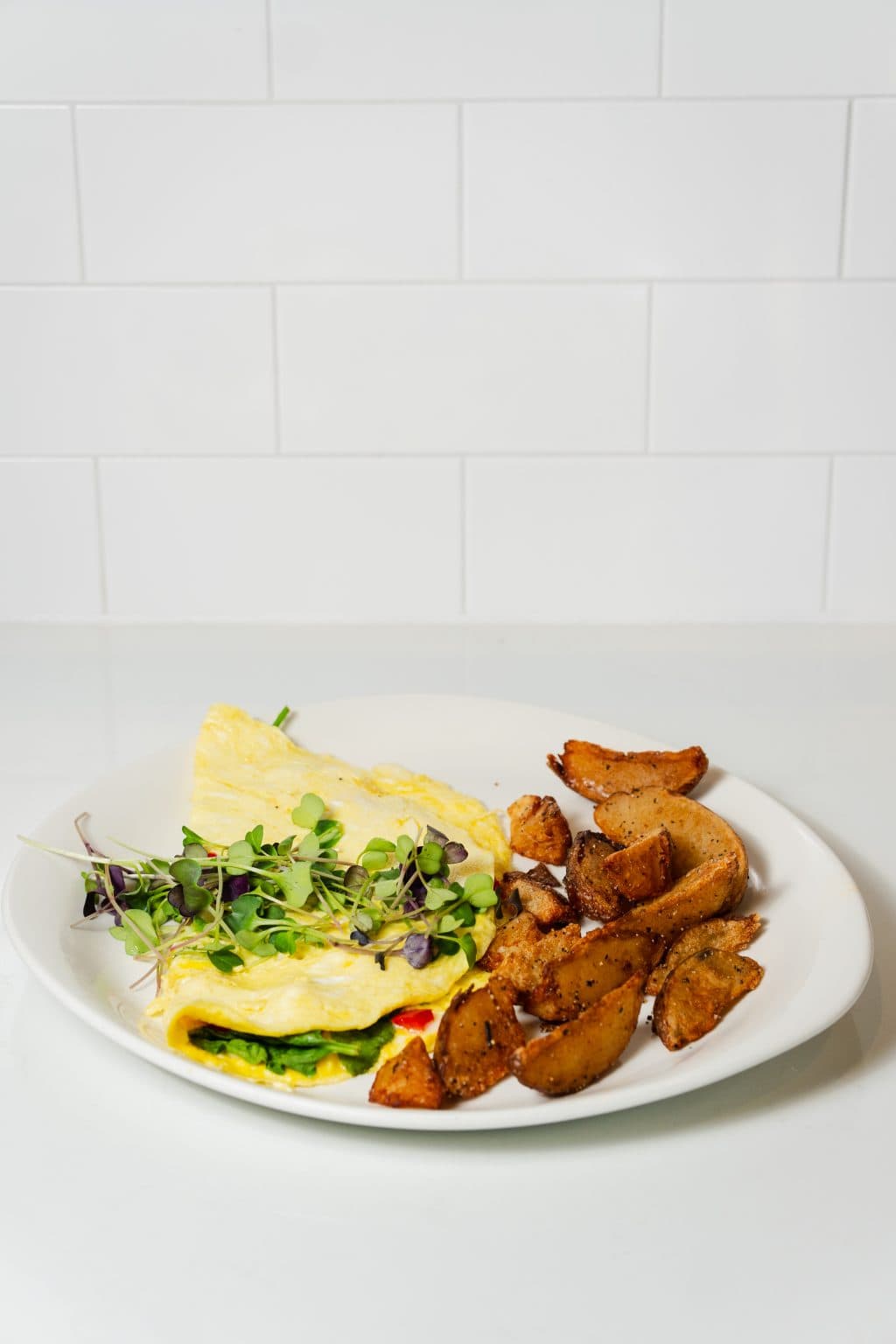 Breakfast plate with omelette, potatoes, and greens on a white dish.
