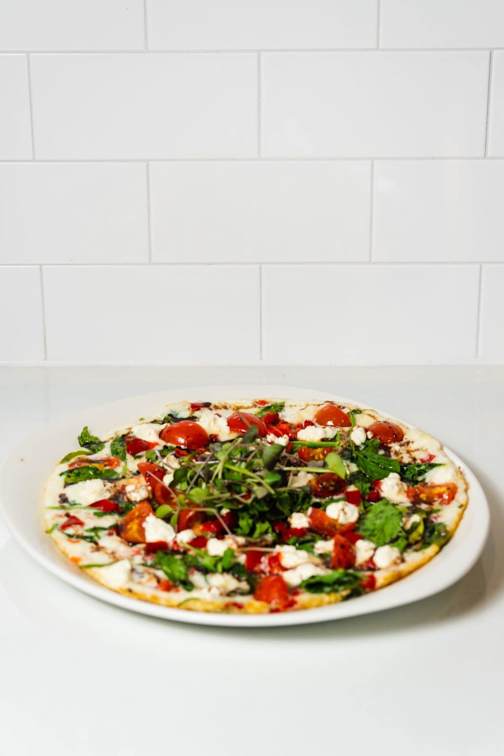 Vegetable pizza with fresh greens, tomatoes, and cheese on a white plate.