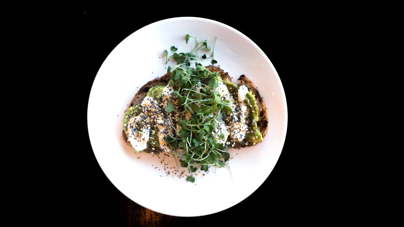 Avocado toast topped with microgreens and sesame seeds on a white plate.
