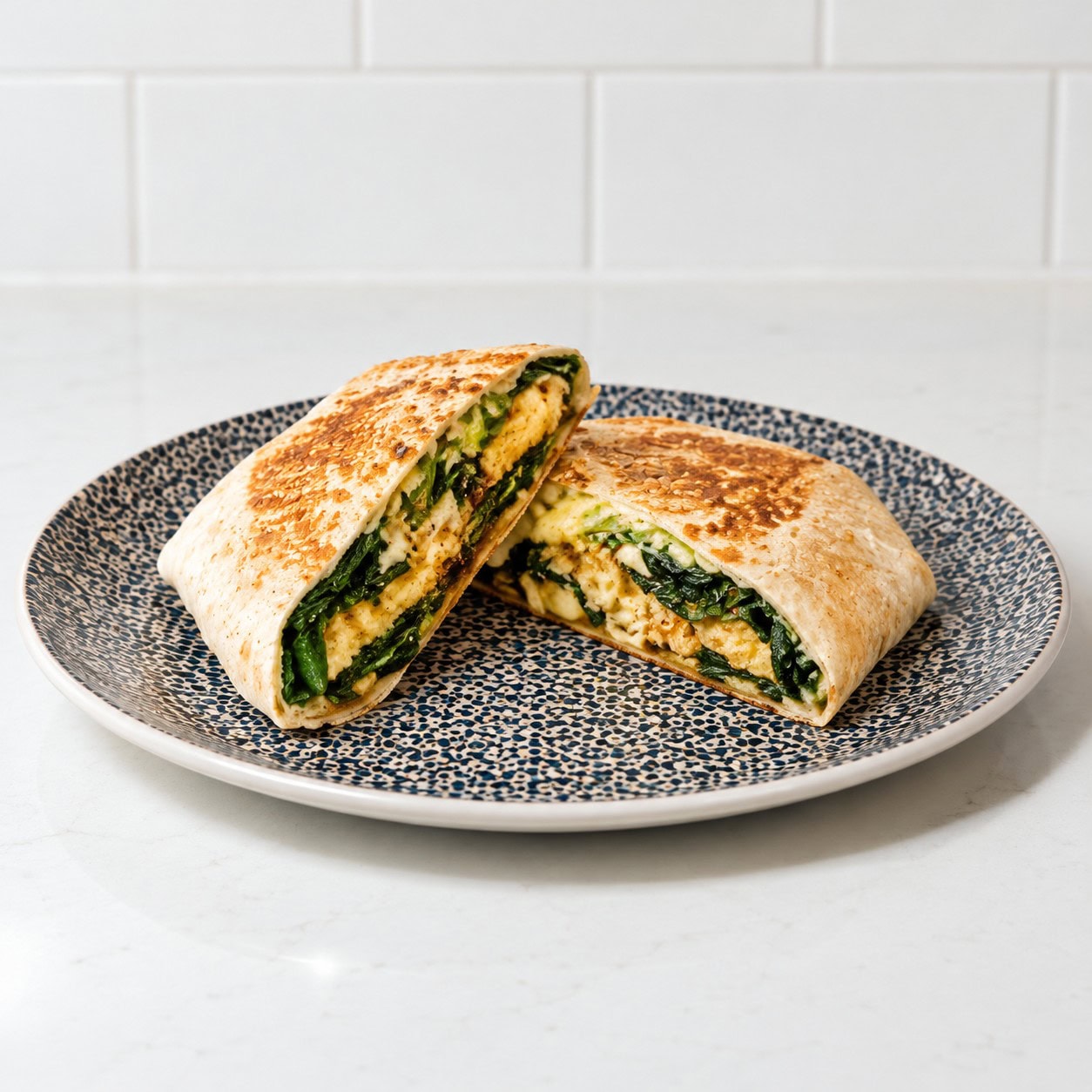 Salmon plate wrap with greens and melted cheese cut in half on a patterned plate.