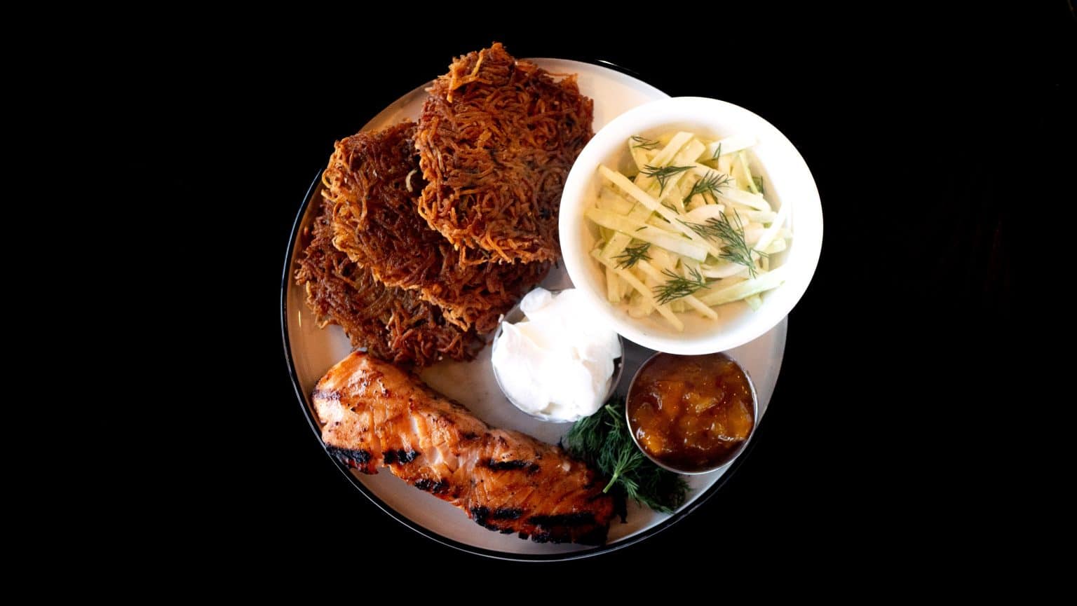 Fried fish with coleslaw, dipping sauce, and side of vegetables on a plate.