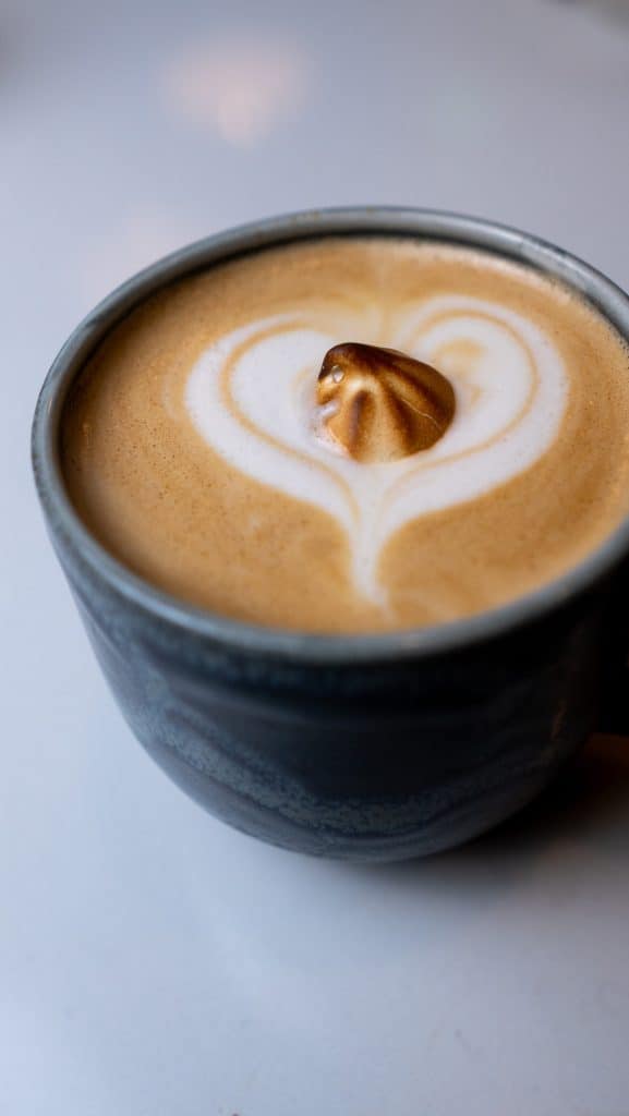 Coffee latte with heart-shaped foam art and caramel topping in a dark ceramic mug.
