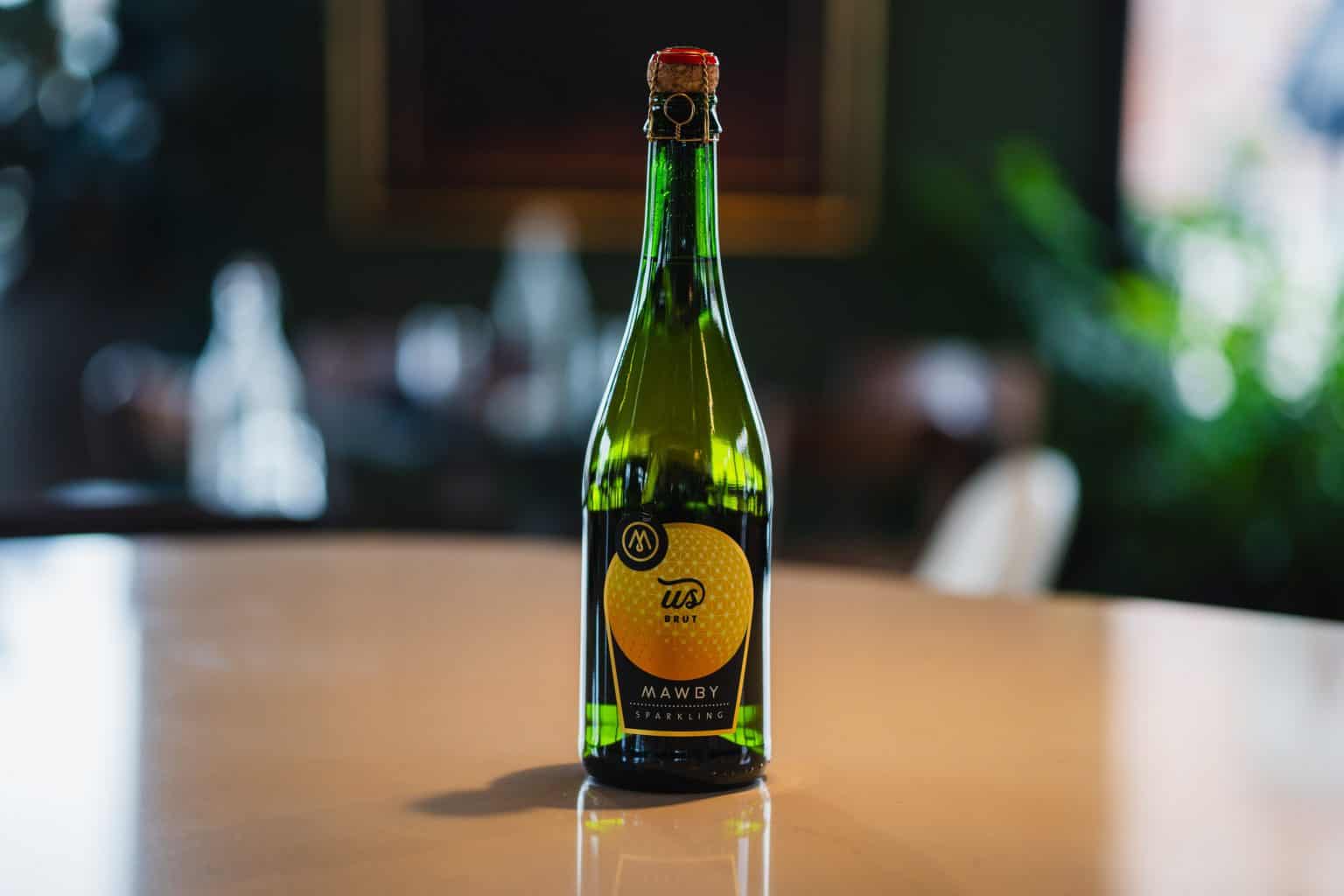 Mudpenny sparkling Mawby bottle on a wooden table, with a blurred background.