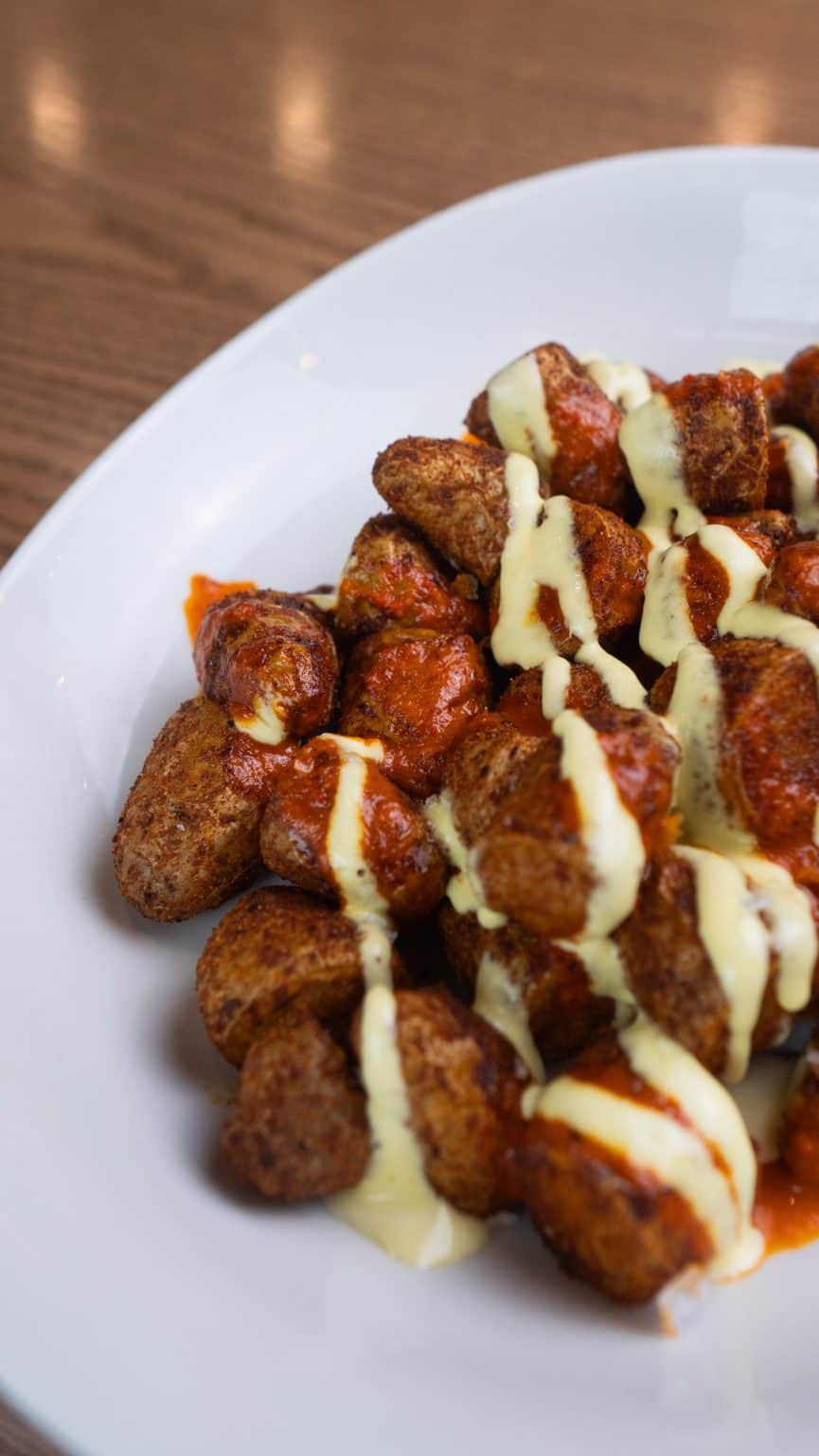 Delicious crispy fried chicken bites drizzled with creamy sauce on a white plate.