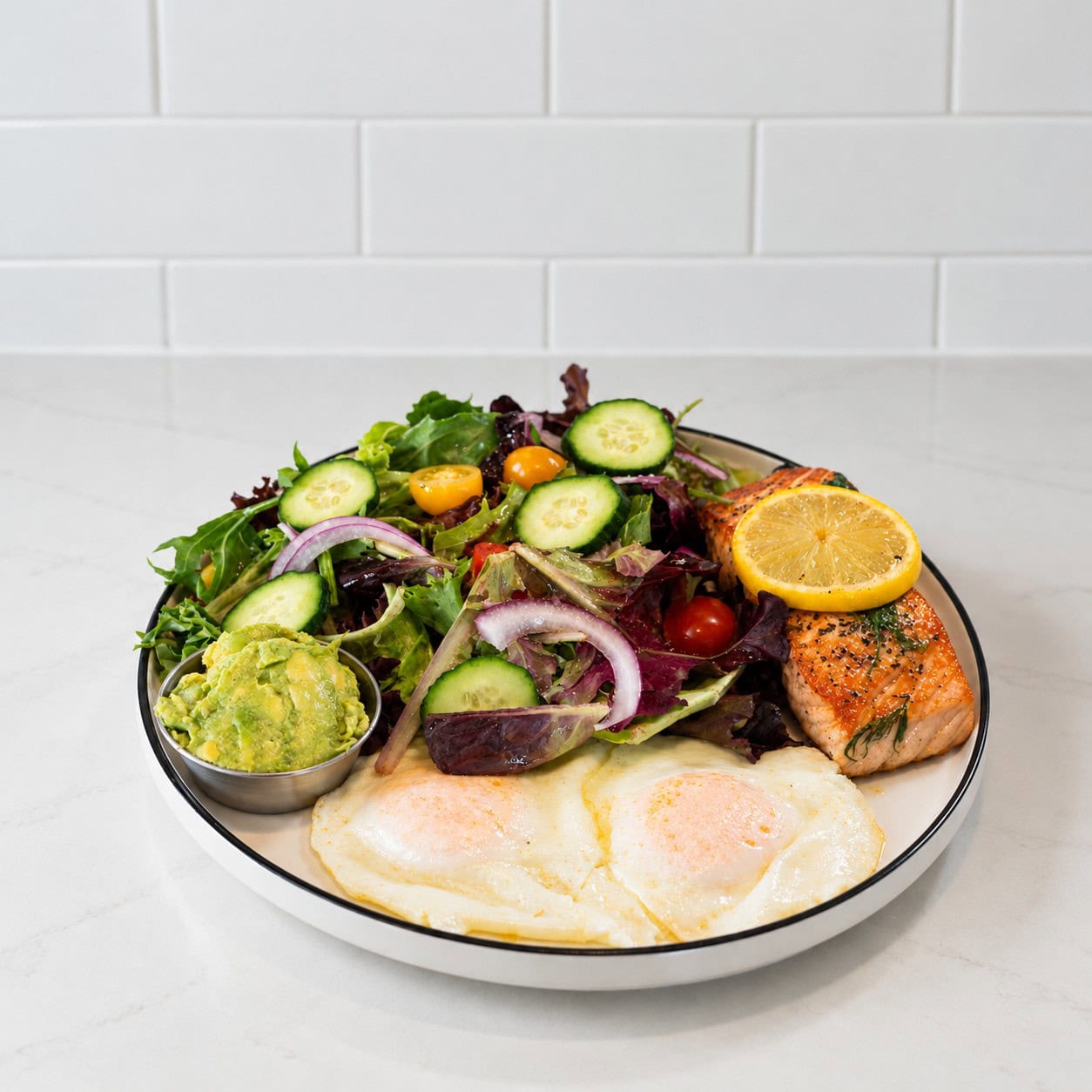 Salmon plate with greens, cucumber, tomatoes, onions, avocado, and citrus.