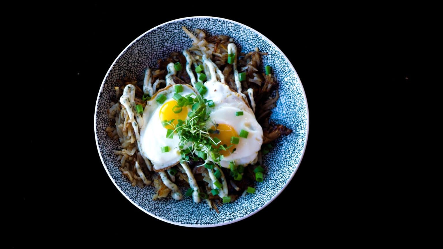 Mushroom pasta with poached egg and herbs in a blue bowl on black background.
