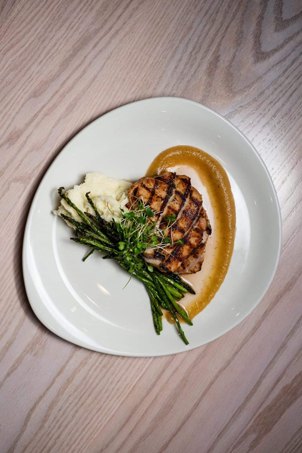 Juicy grilled pork chop served with green beans, mashed potatoes, and gravy on a white plate.
