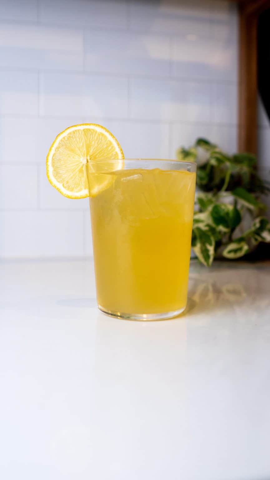 Refreshing glass of lemonade with lemon slice on a white countertop.
