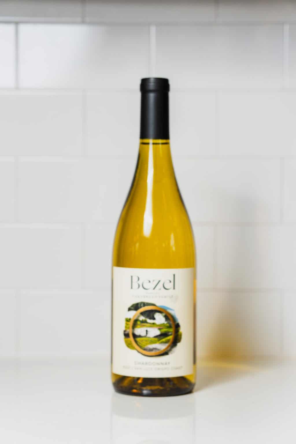 Yellow Chardonnay wine bottle with black cap and label on white background.