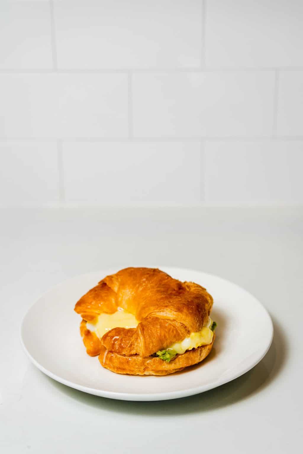 Breakfast sandwich on a croissant with egg, cheddar, and avocado.