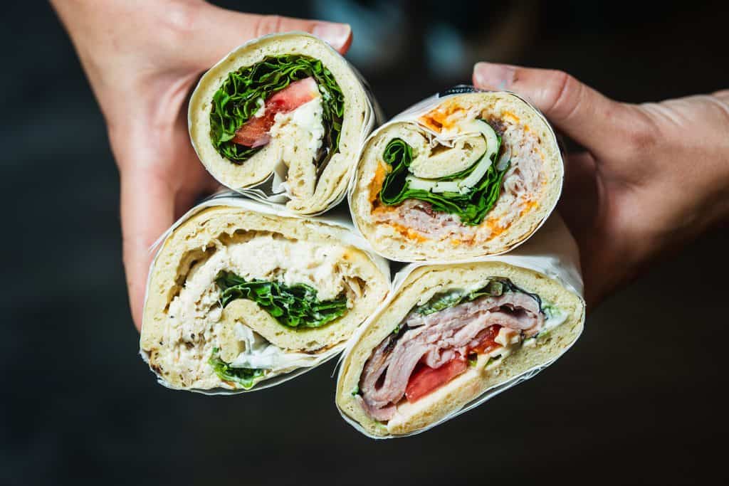 Assorted fresh wraps with greens, turkey, and tomatoes held together.