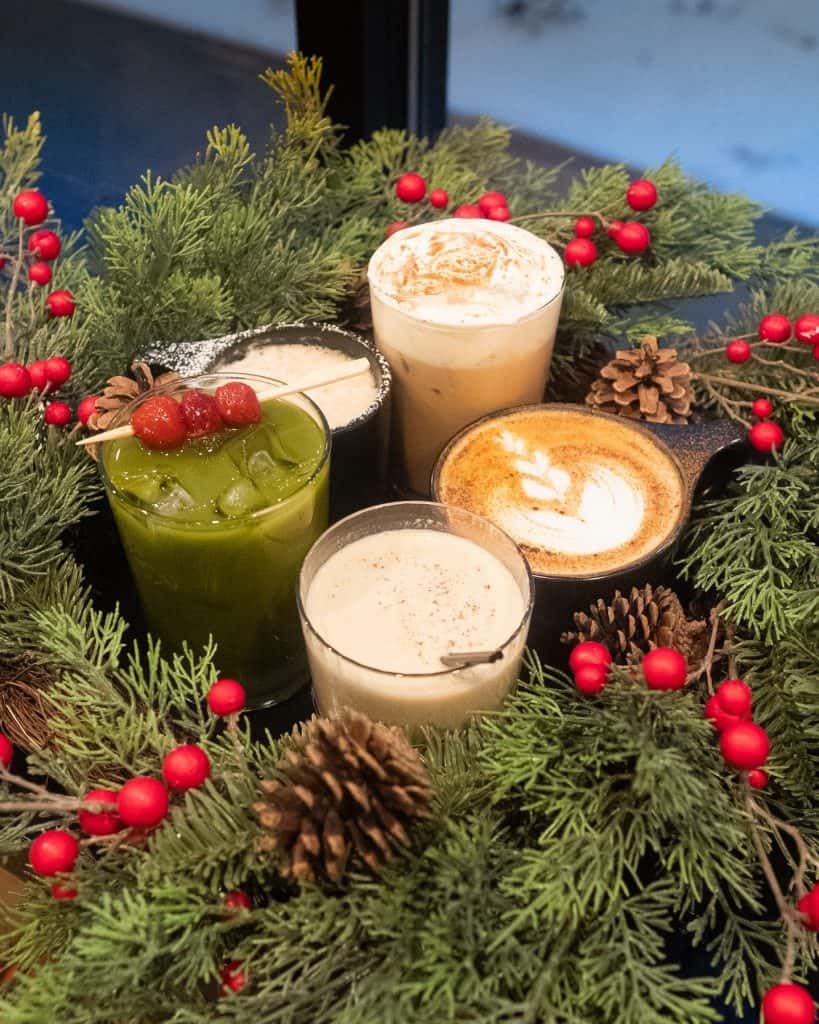 Festive holiday coffee drinks surrounded by pine branches and red berries.