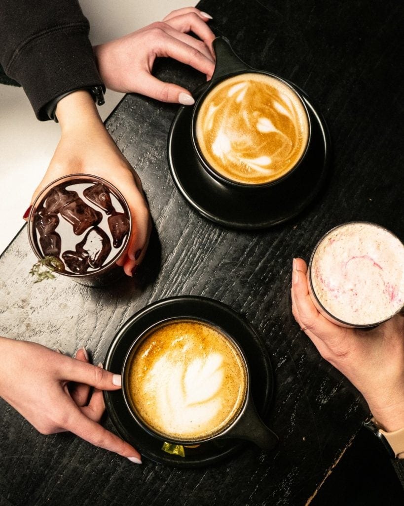 Coffee drinks with ice, foam art, and colorful toppings on dark wooden table.