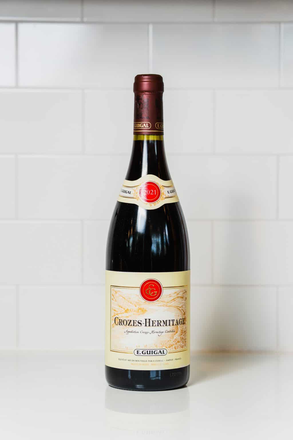 Bottle of Crozes-Hermitage red wine on white tiled background.