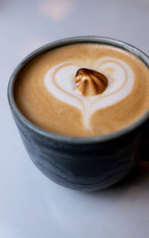Latte art with heart shape and nut topping in a ceramic cup, close-up view.