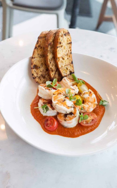 Delicious shrimp served on a rich tomato sauce with fresh herbs, accompanied by toasted bread slices.