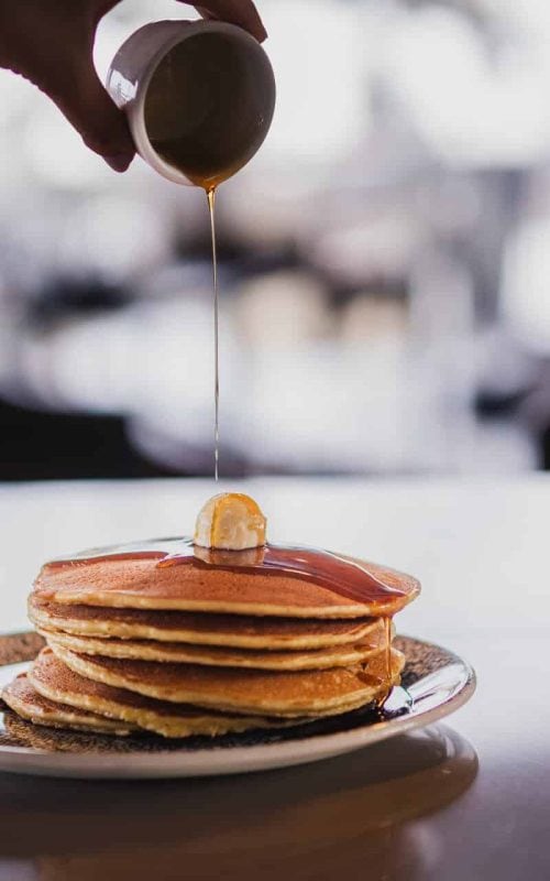Stack of fluffy pancakes drizzled with syrup and topped with a pat of butter.