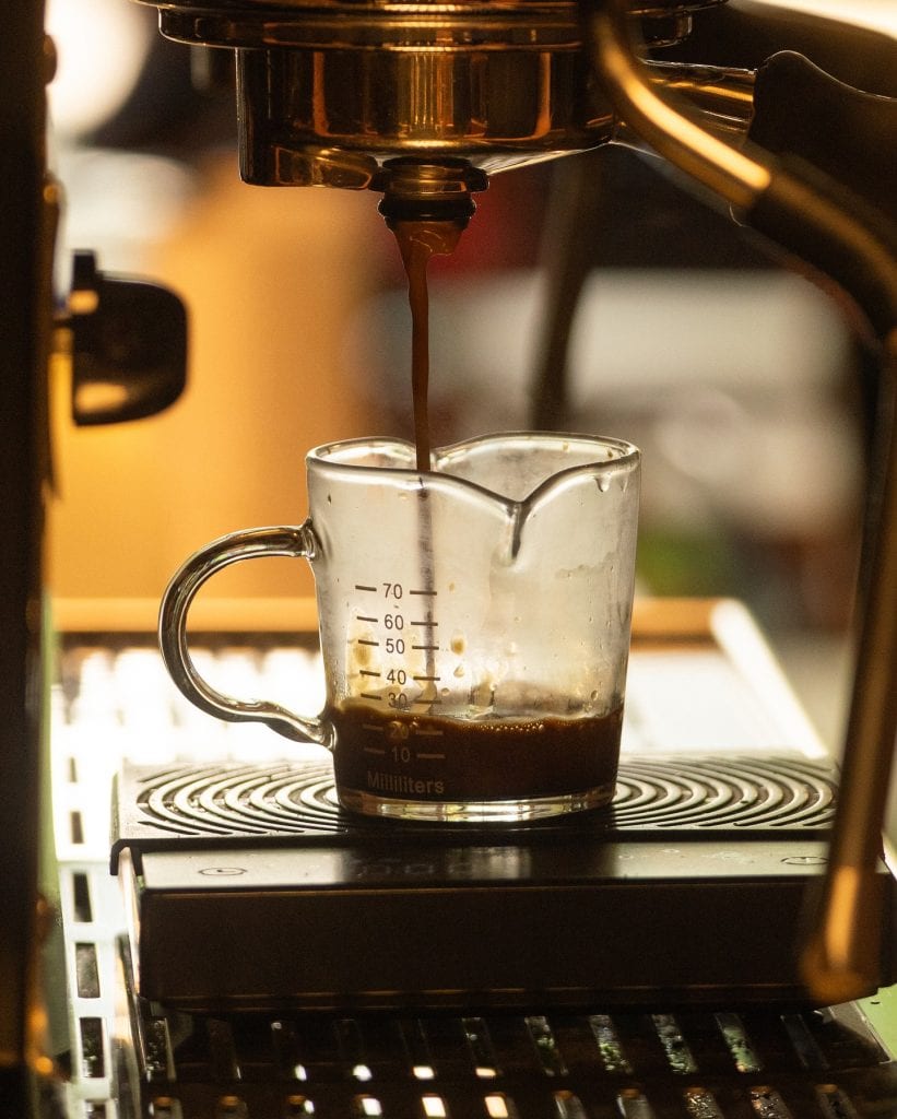 Freshly brewed coffee being extracted into a glass mug on a coffee machine.