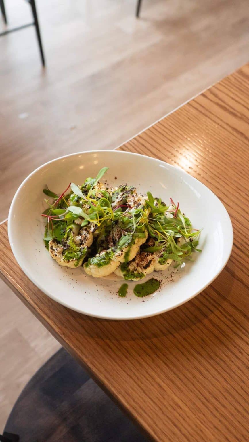 Fresh gourmet salad with greens, herbs, and dressing served on a white plate at Mudpenny.