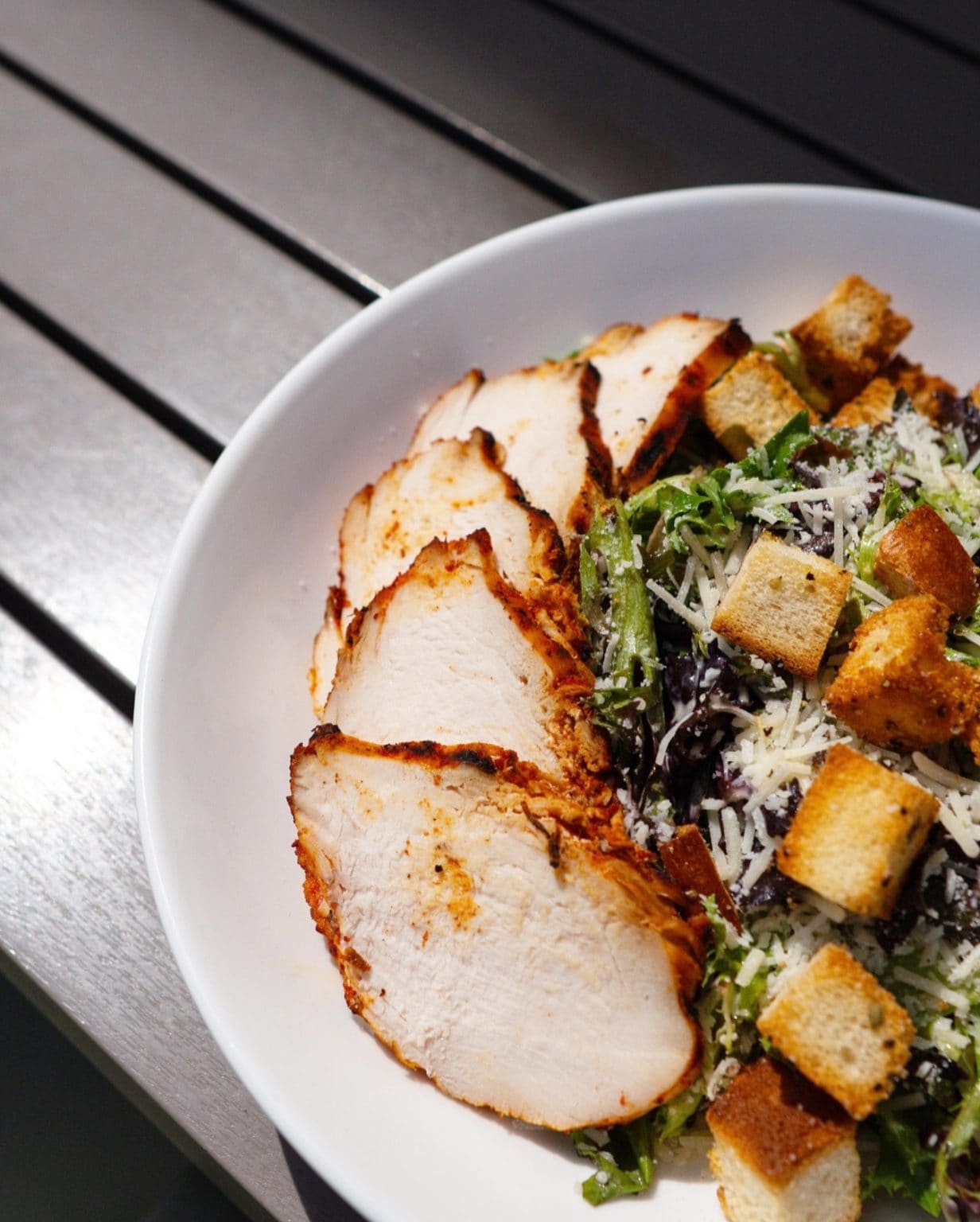 Fresh grilled chicken salad with greens, croutons, and cheese in a white bowl.