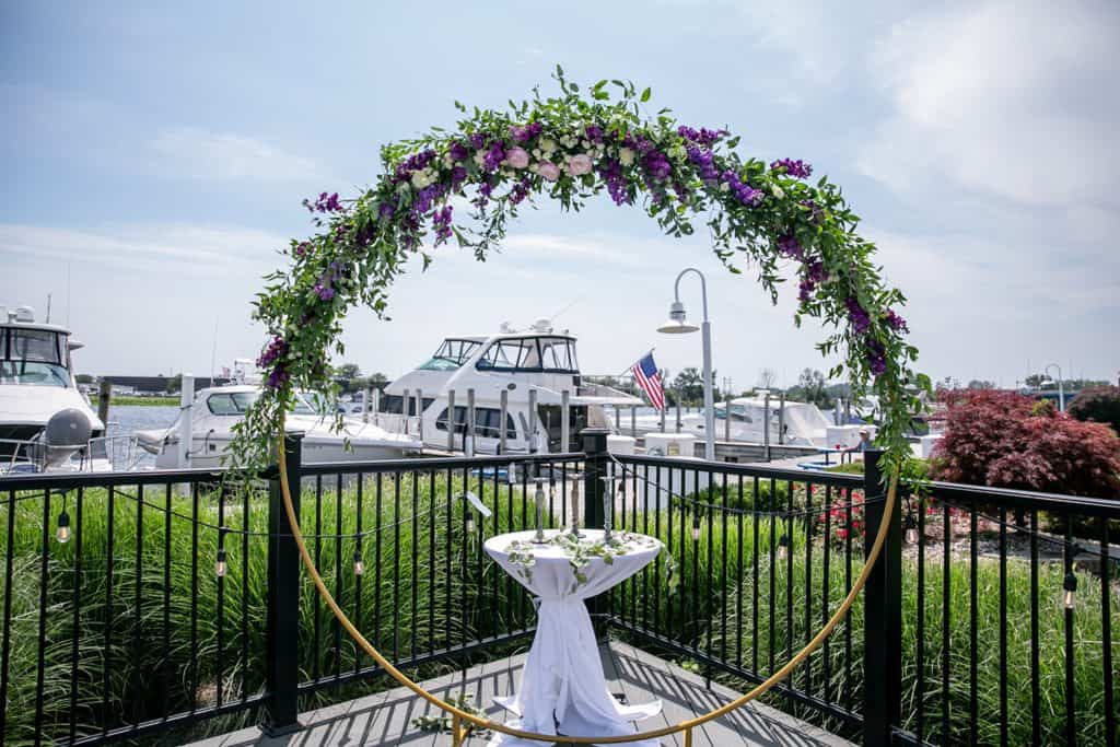 Charming floral arch with purple and white flowers overlooking marina for private events.