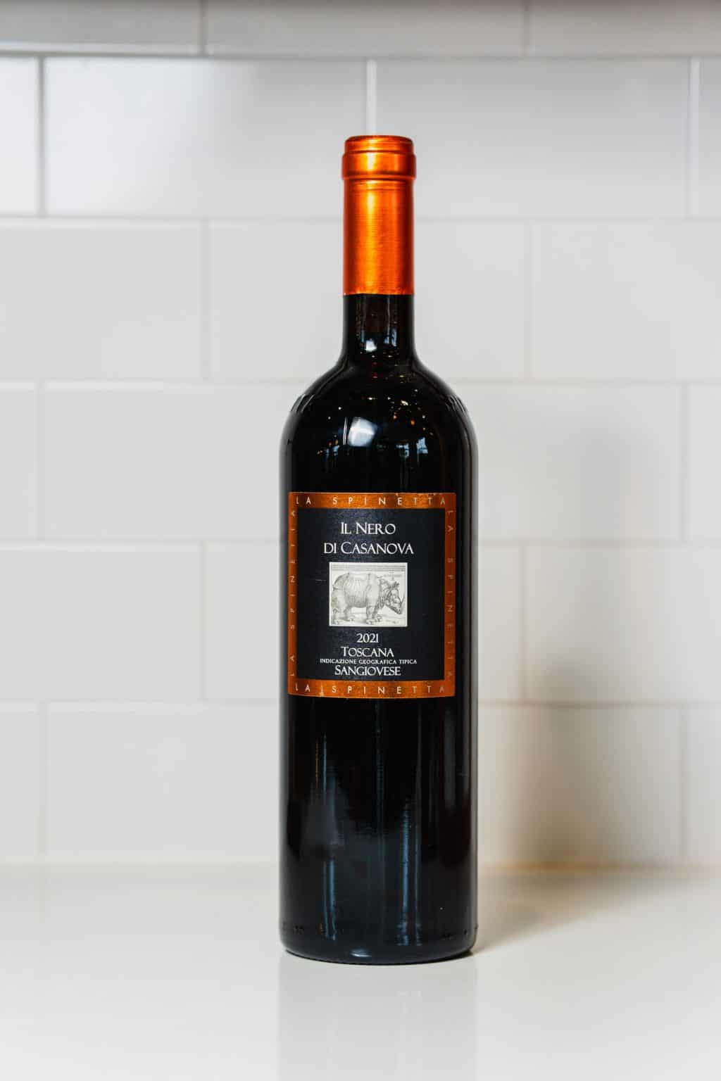 Elegant bottle of Il Nero di Casanova red wine on white tiled background.