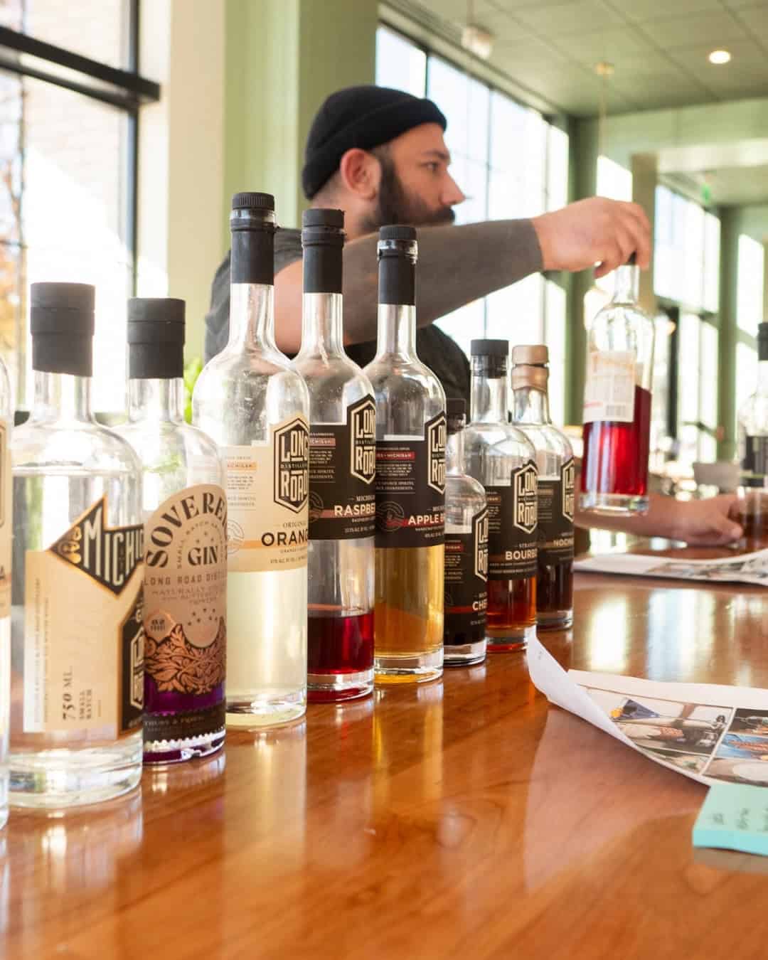 Tasting various gin bottles at Mudpenny bar with a bartender in the background.