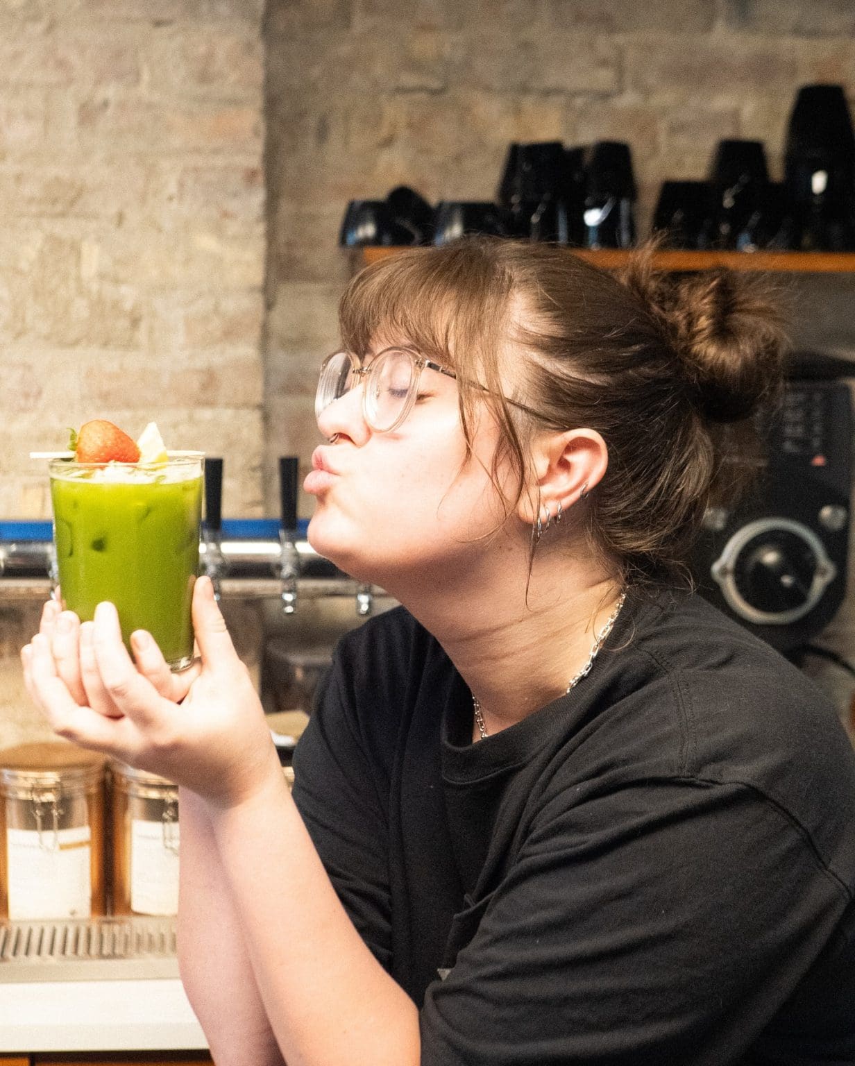 Green smoothie with strawberries, held by a woman with glasses.