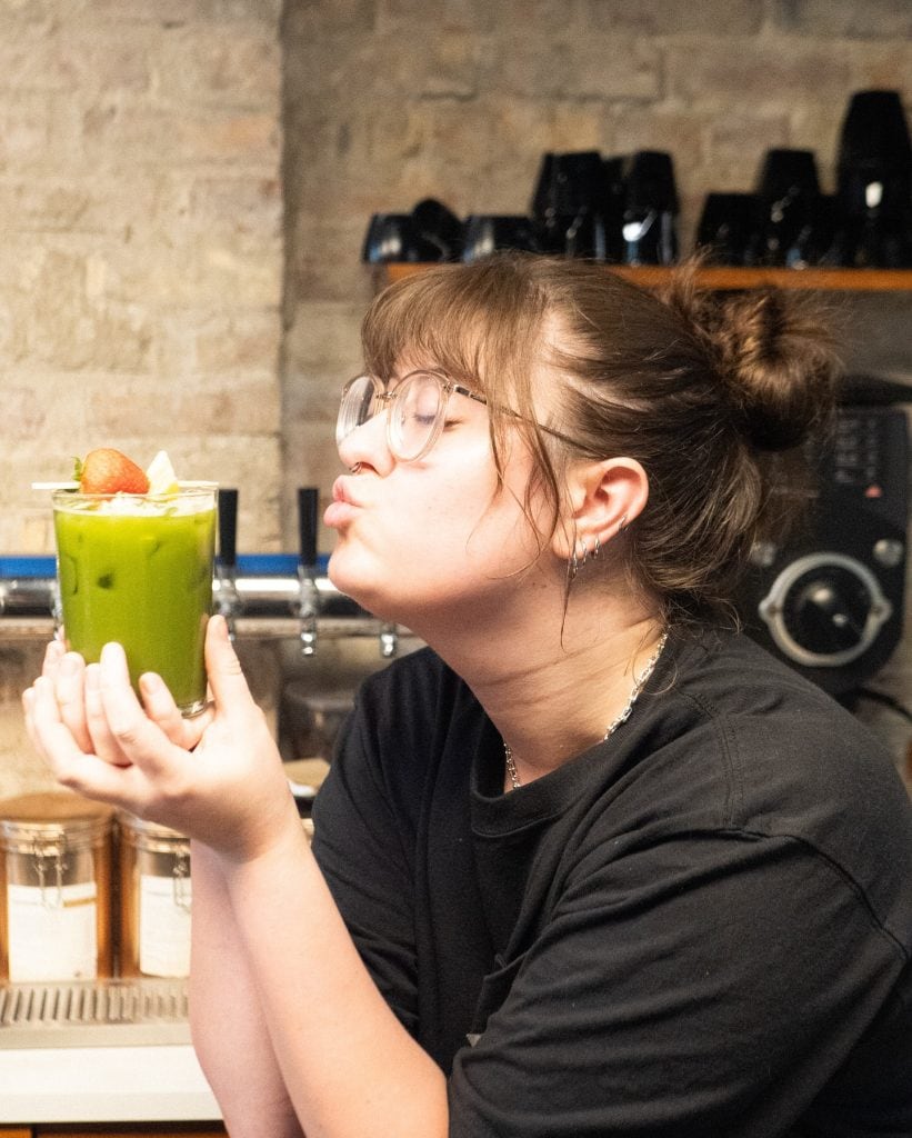 Green smoothie with strawberries, held by a woman with glasses.