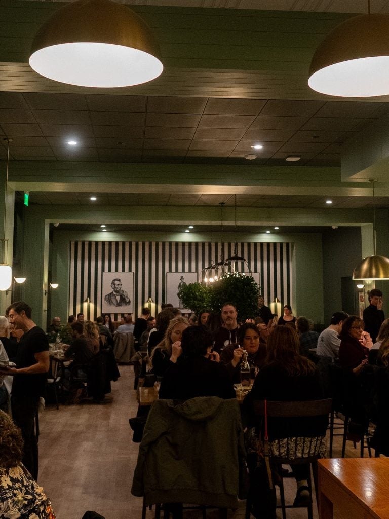 Cozy restaurant interior filled with guests enjoying meals and conversations, warm lighting, and sty.