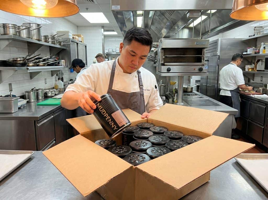 A chef in a commercial kitchen packs food into containers for wholesale orders.