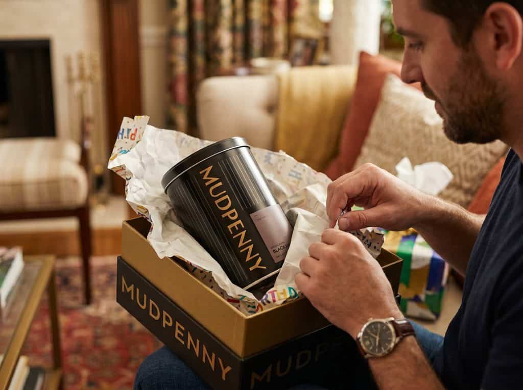 Man opening Mudpenny coffee subscription gift box at home.
