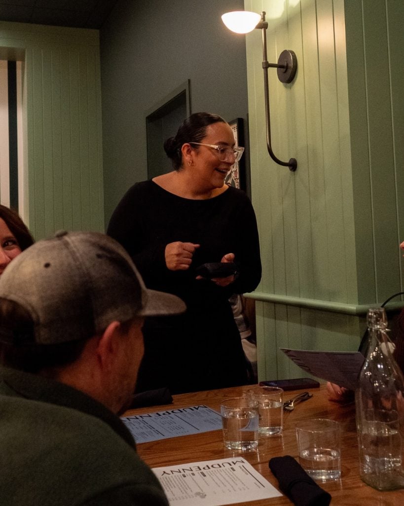 Woman smiling and using her phone during a coffee shop gathering with friends.