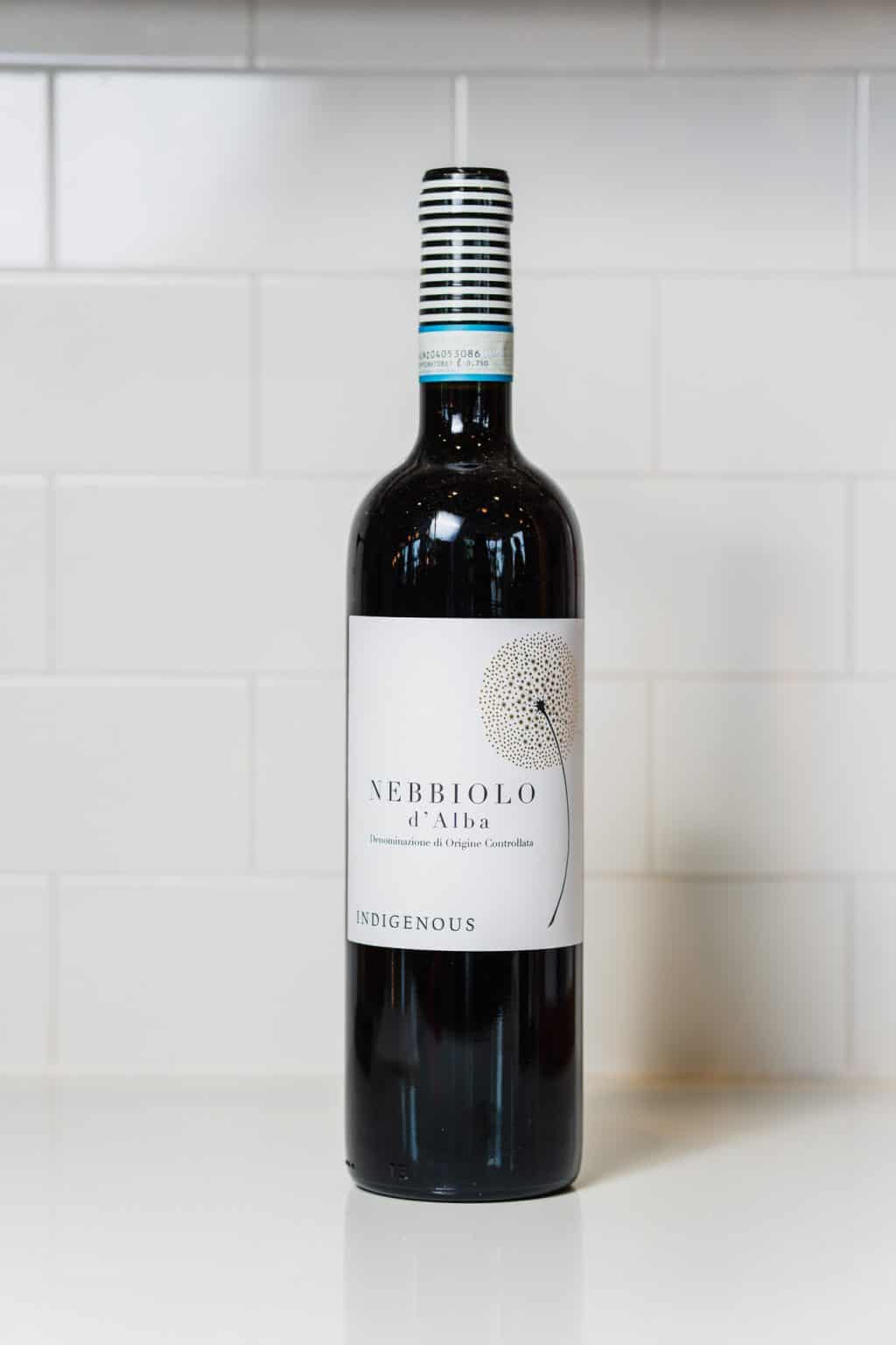 Bottle of Nebbiolo d'Alba wine on a white surface with white tiled background.
