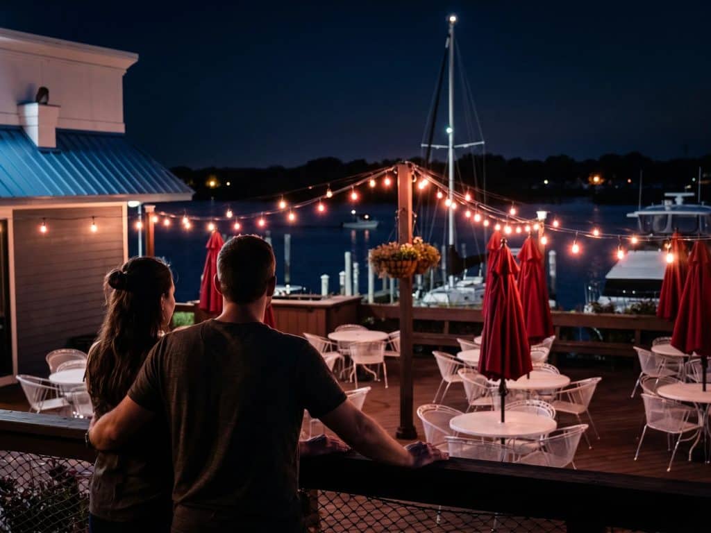 Alfresco dining at Spring Lake with string lights and boats in the background.