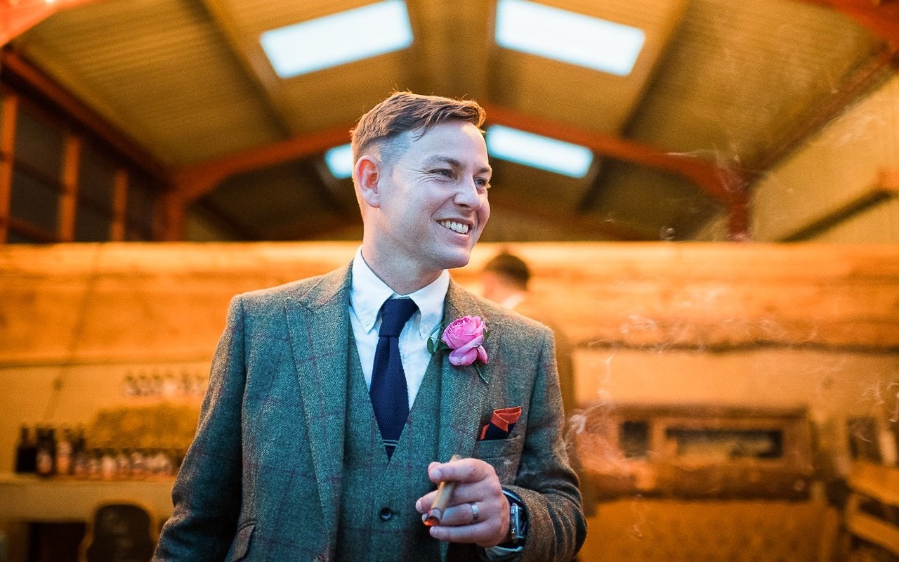 Dorset barn farm wedding groom tweed three piece wedding suit smoking a cigar