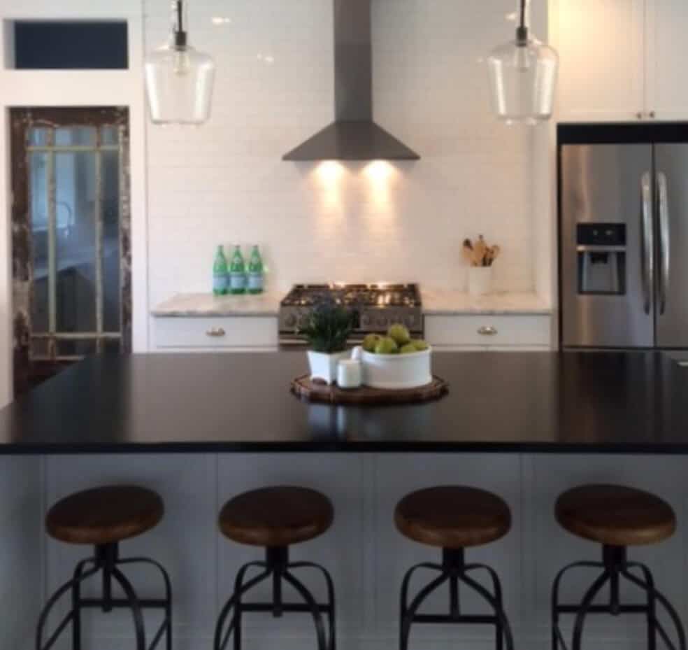 Kitchen with black granite island, white cabinets, stainless steel appliances, and pendant lighting.